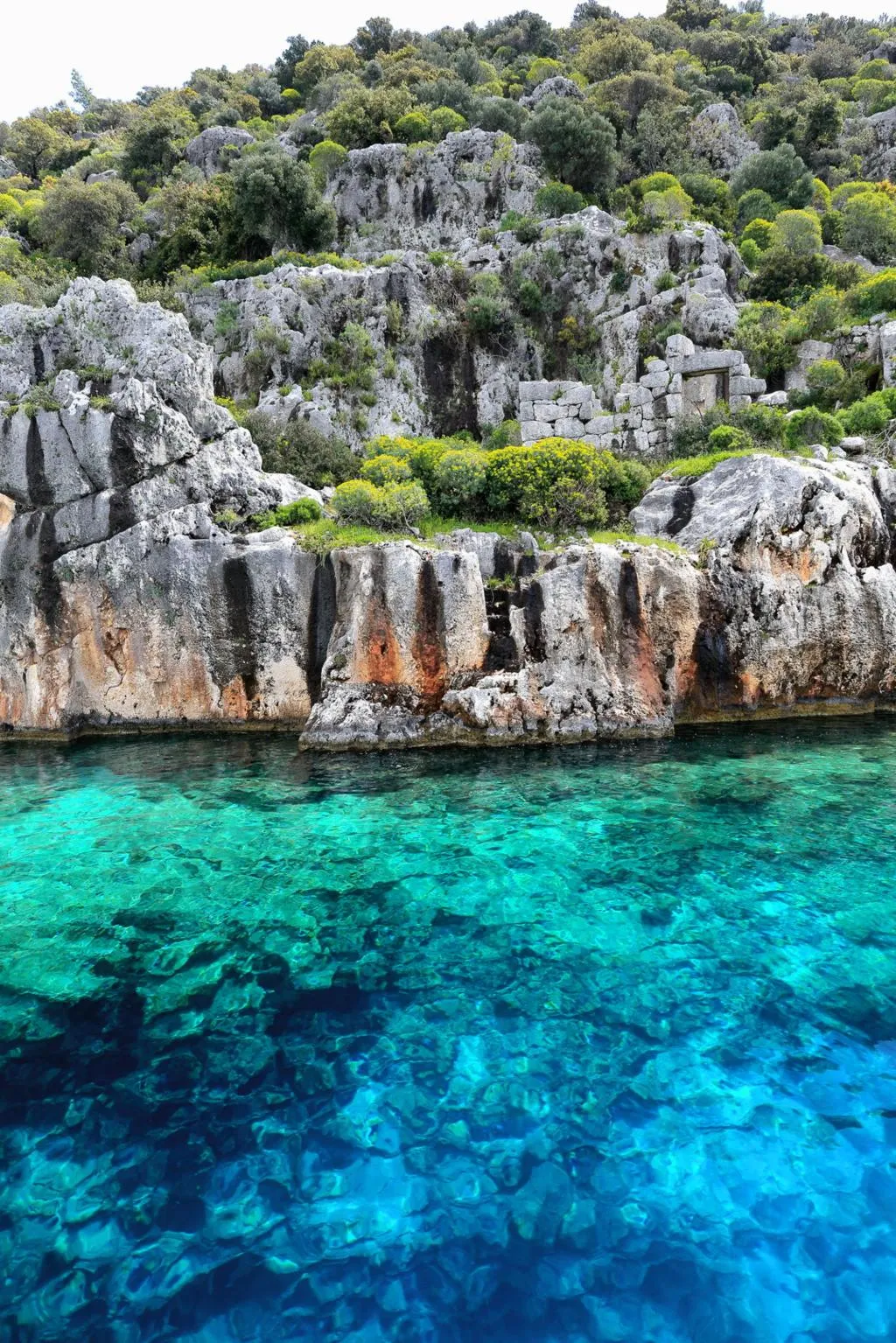 Rocky shore and clear turquoise water where the ruins of Aperlai meet the sea