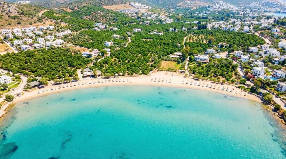 The turquoise water and sandy beach of Bitez Bay with tangerine groves behind