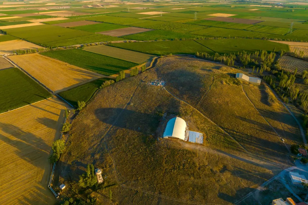 Aerial view of the Çatalhöyük mound and its shelters among green fields