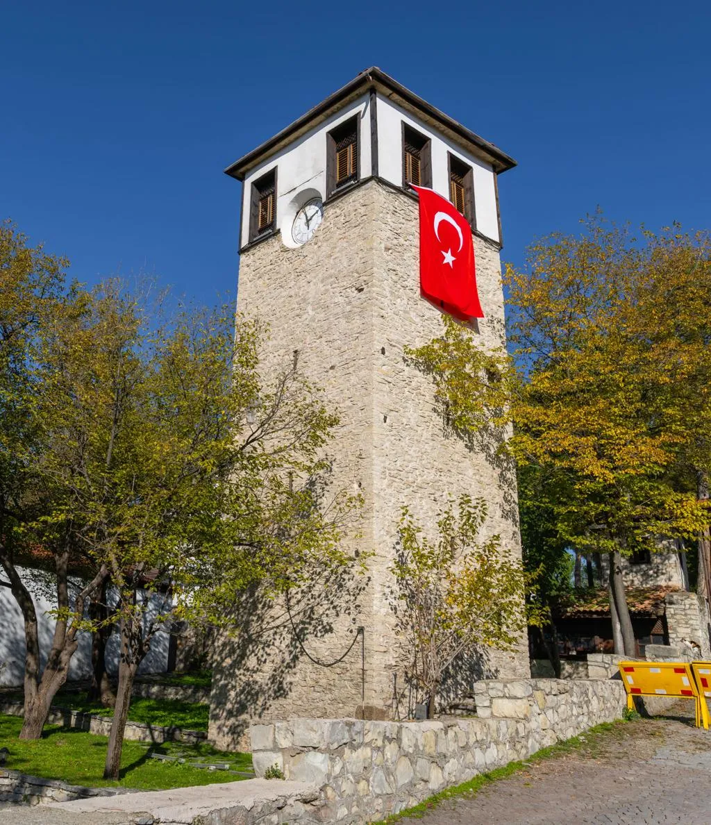Safranbolu's stone clock tower with a Turkish flag among autumn trees