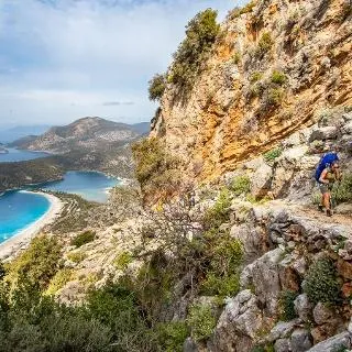 A walker on a rocky cliff path with the Ölüdeniz lagoon far below