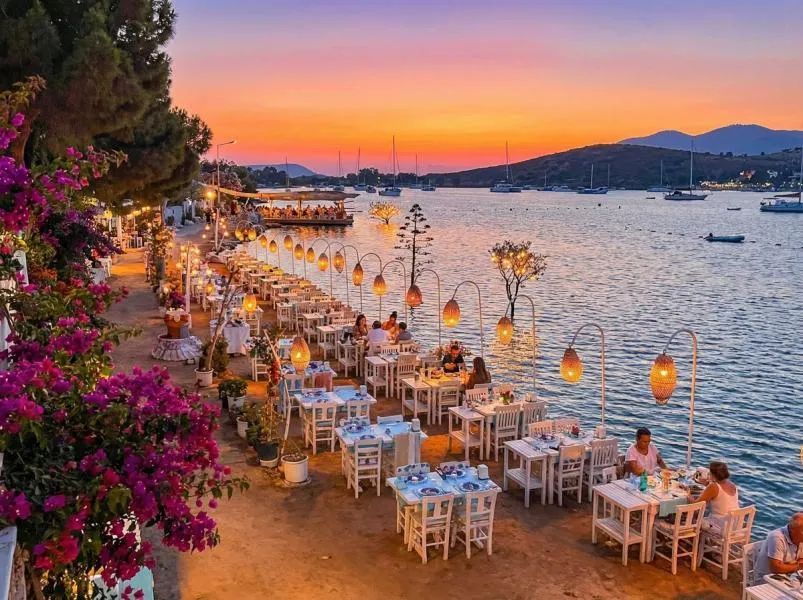 Restaurant tables with lanterns along the water at sunset on the Bodrum peninsula