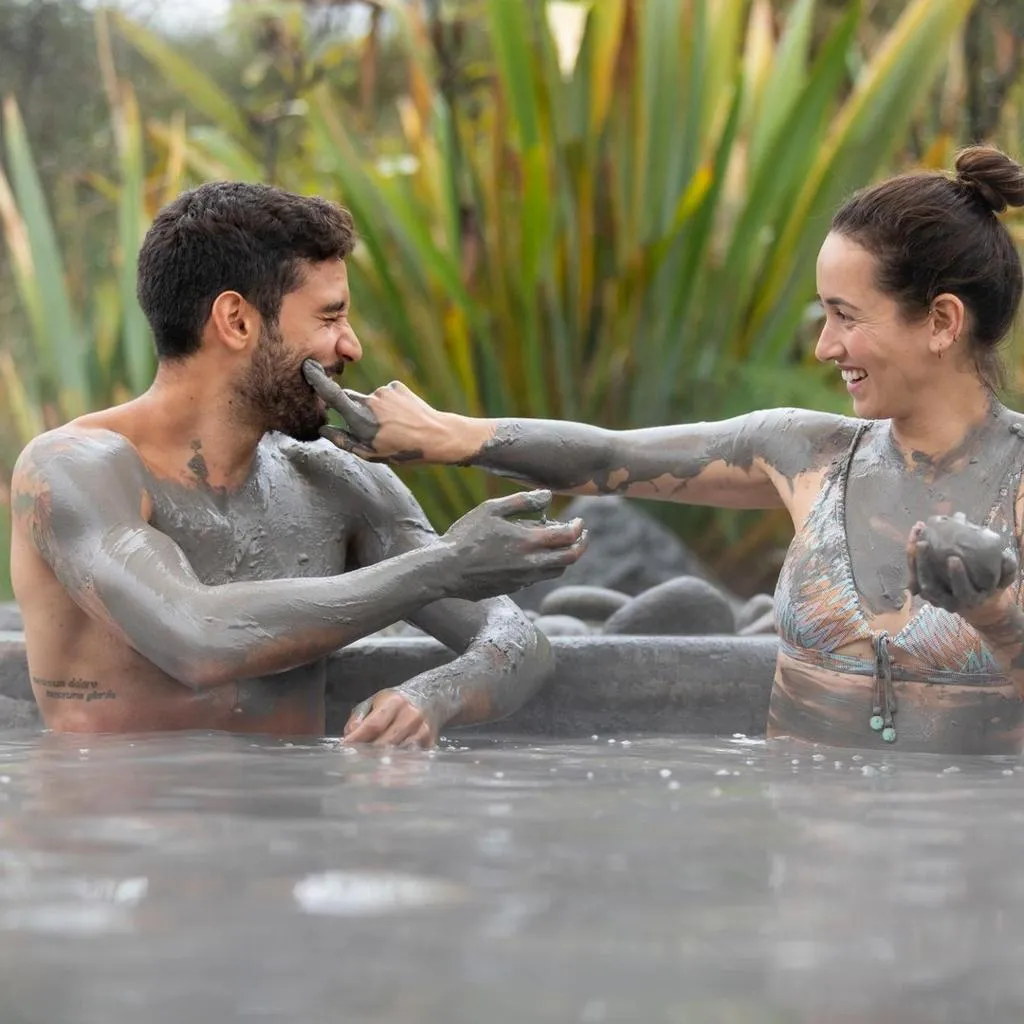 A smiling couple covered in grey mud in a mud bath