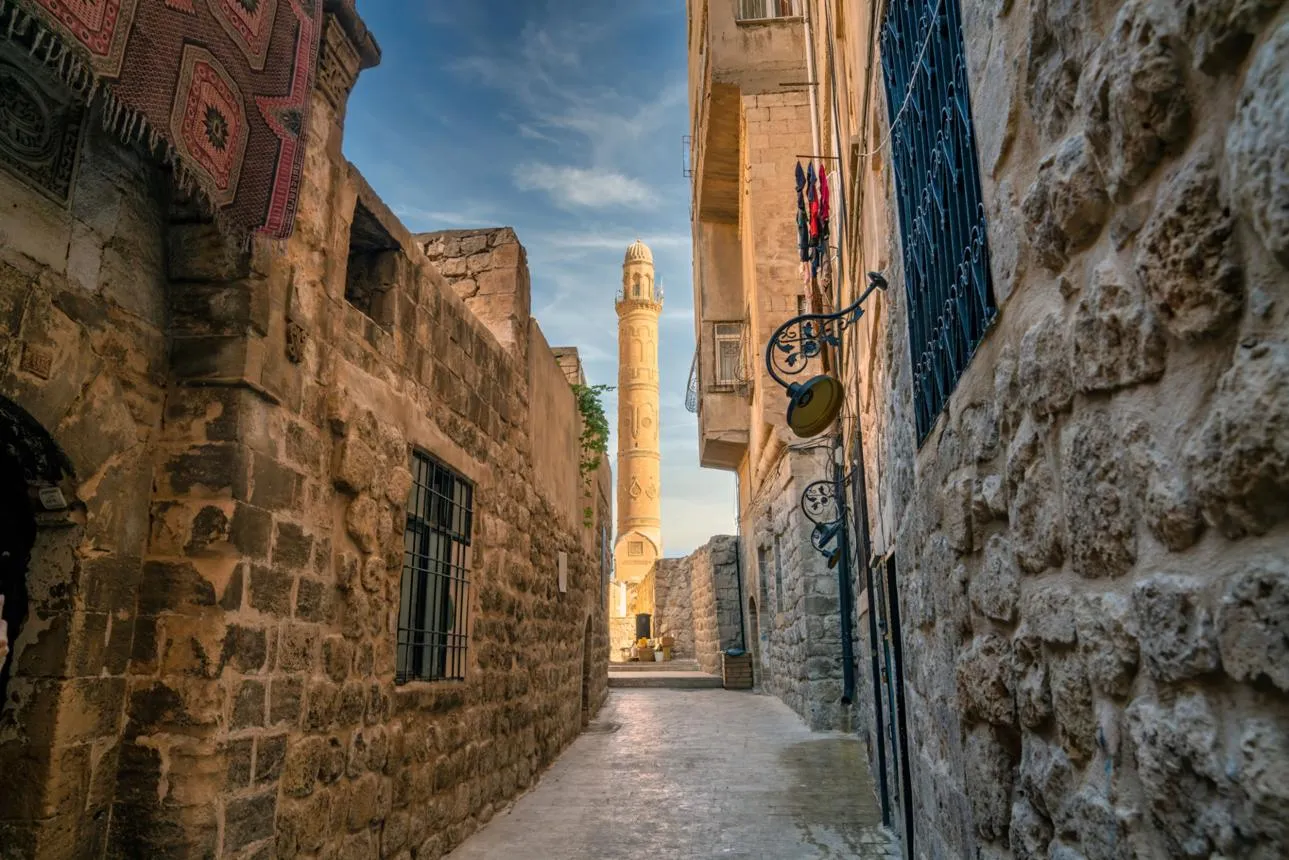 A narrow stone lane in Mardin's old town with the minaret of Ulu Cami at the end