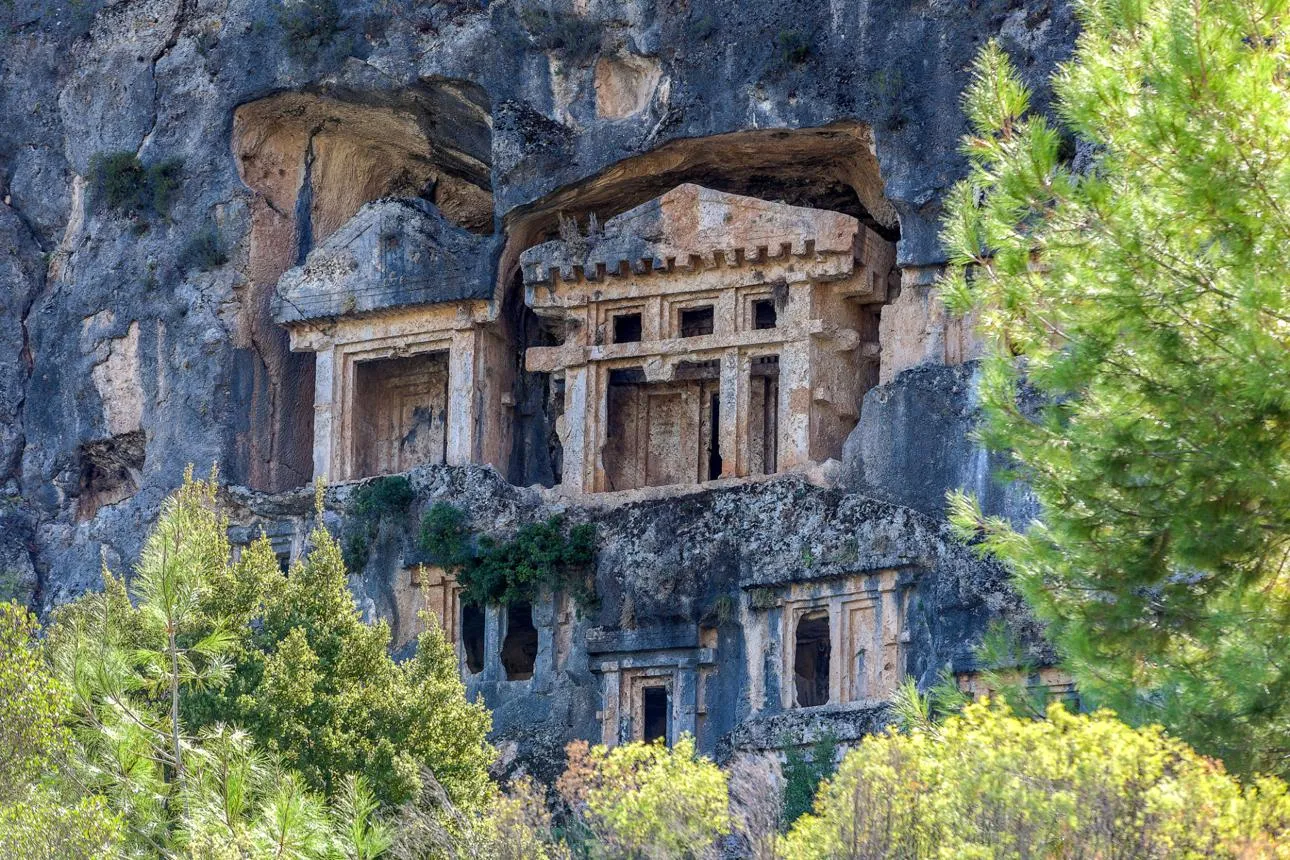 A temple-fronted Lycian rock tomb at Pınara among green trees
