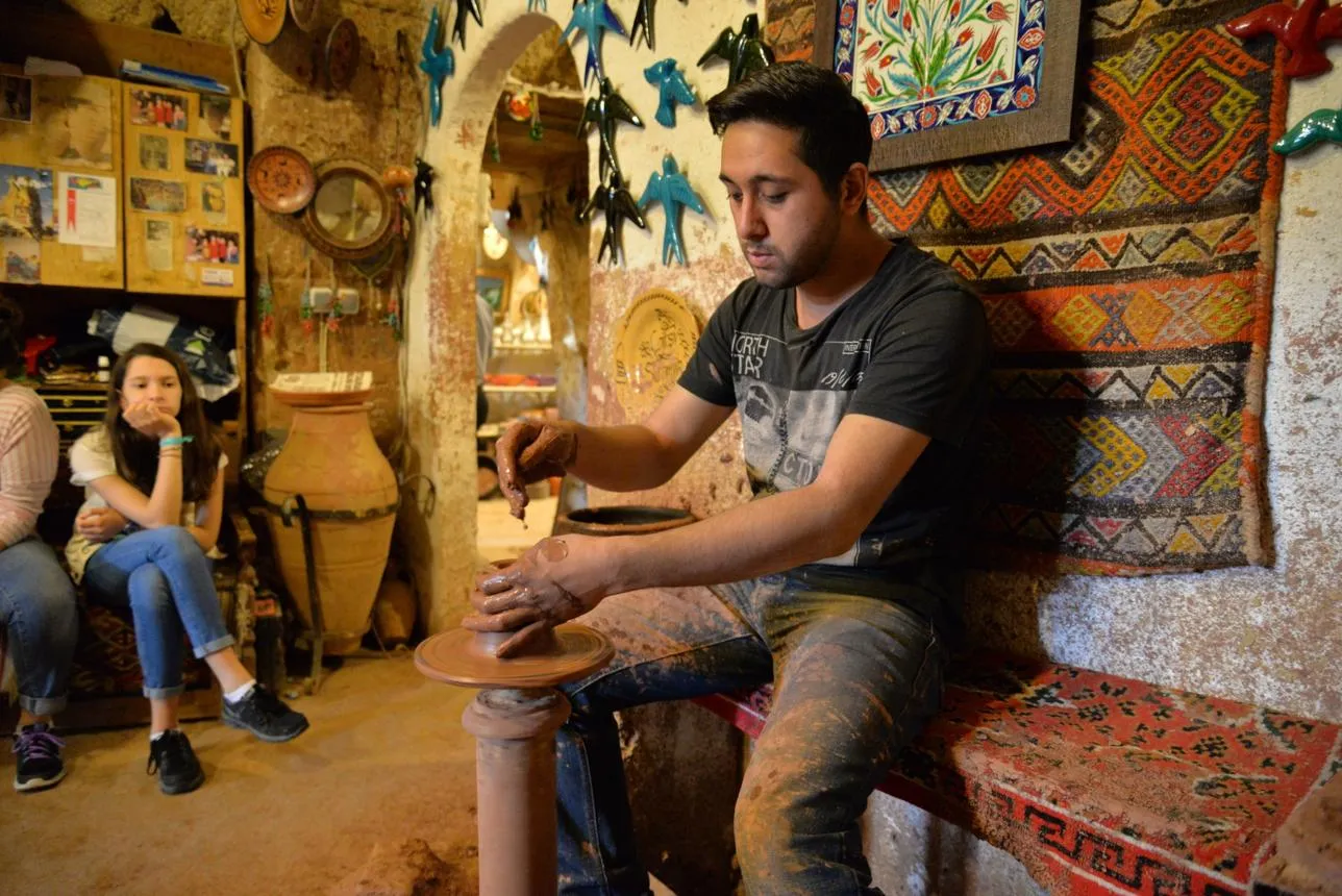 A potter at the wheel in a cave workshop, watched by visitors