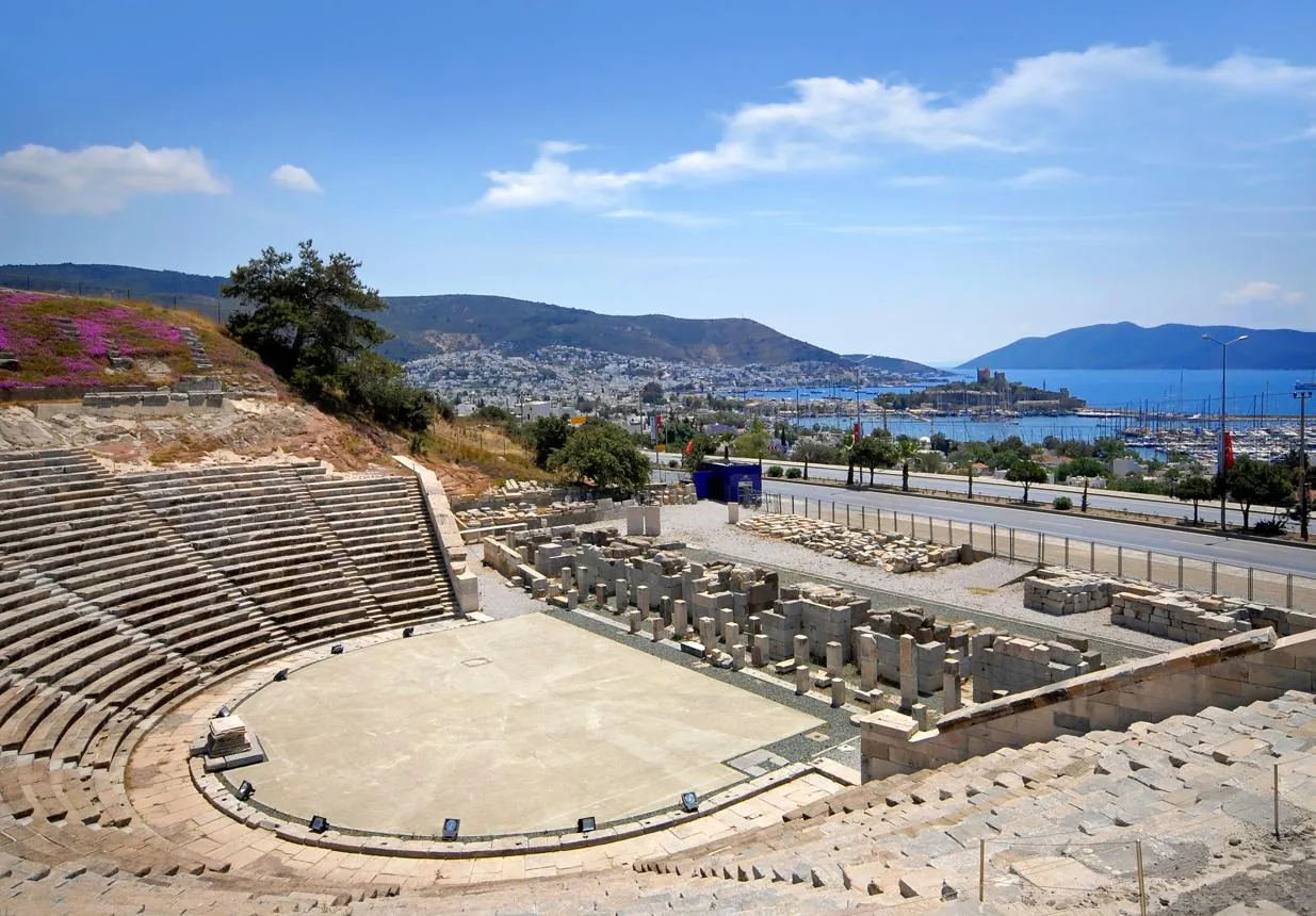 Stone seats of the ancient theatre with the castle and harbour in the distance
