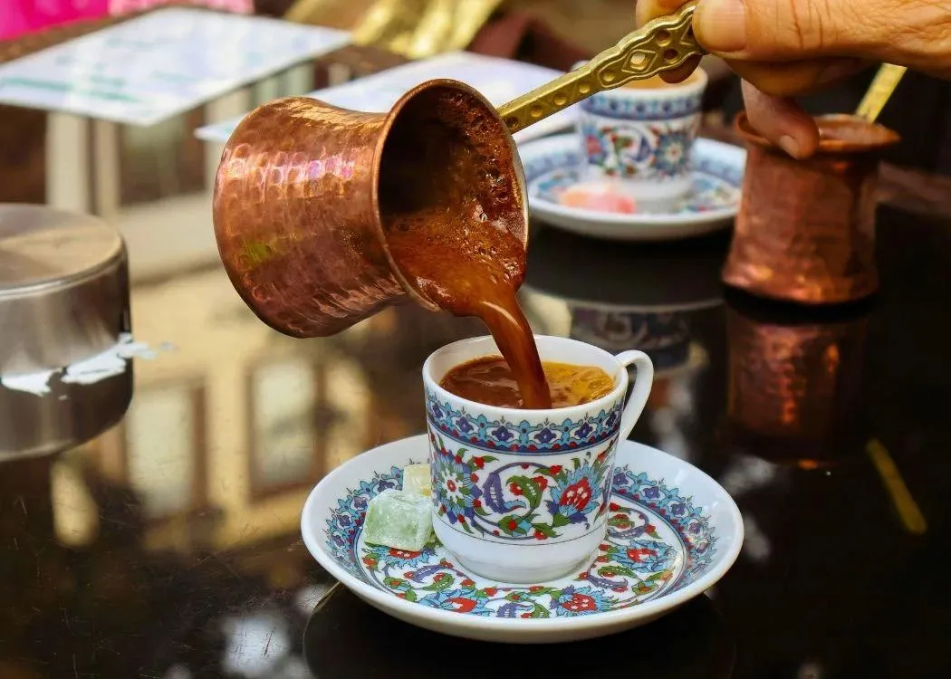 Turkish coffee poured from a copper pot into a decorated cup