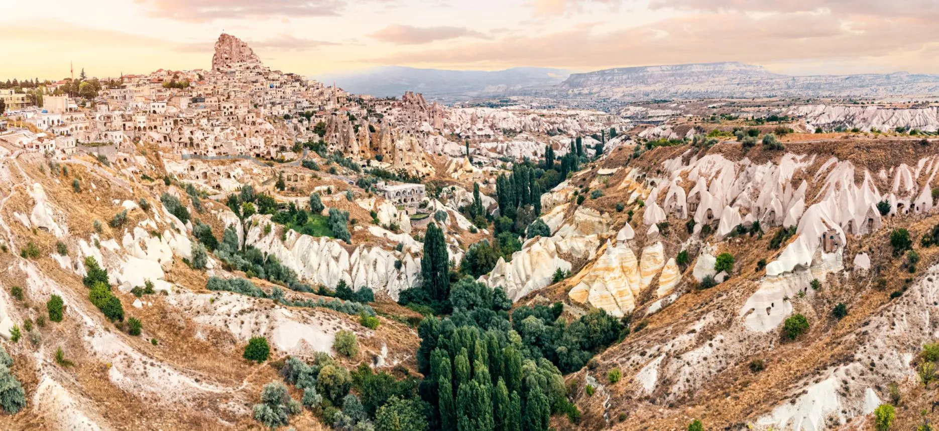 Uçhisar Castle above a valley of white rock formations at sunset