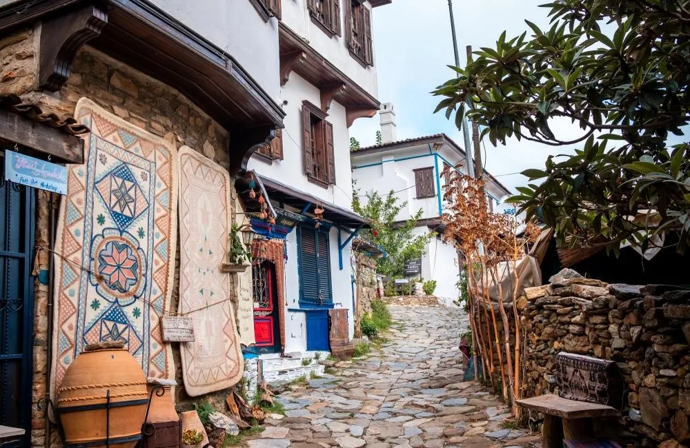 A cobbled lane of Şirince with whitewashed houses, wooden shutters and hand-painted rugs