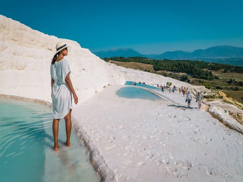 A traveller in a sun hat standing barefoot in a shallow pool on the Pamukkale terraces